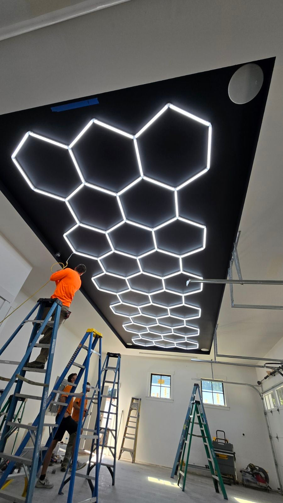 Installer on a ladder mounting a hexagon LED light grid to a garage ceiling