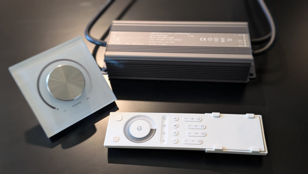 Glass rotary wall dimmer with a brushed-metal knob, dark aluminum LED driver and white handheld remote, front view