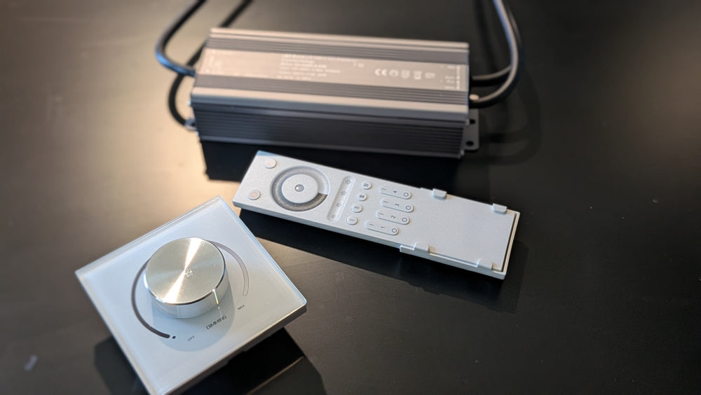 Glass rotary wall dimmer, dark aluminum LED driver and white handheld remote, angled view