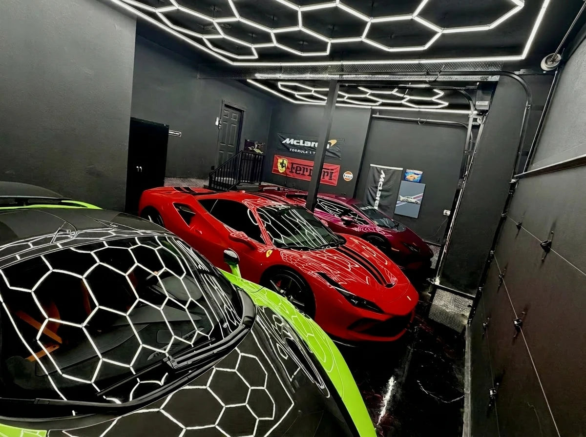 A high-end garage or showroom with dark gray walls and a distinctive hexagonal LED light grid on the ceiling. In the foreground, the hood of a black sports car with neon green accents is visible, reflecting hexagon ceiling lights.